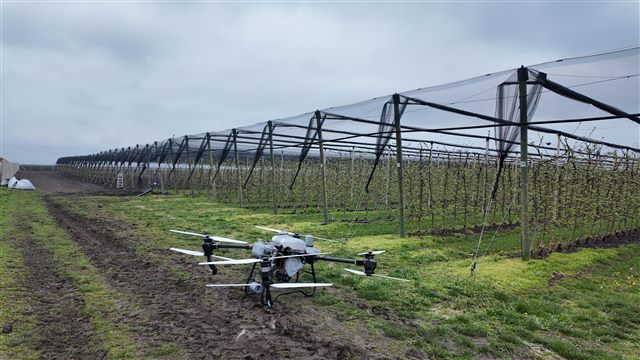 Poljoprivredni dron pored voćnjaka sa protivgradnom konstrukcijom